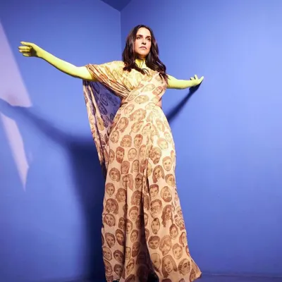 A full-length view of this artistic ensemble. The flowing, printed fabric paired with bright neon gloves creates a look that is both a fashion statement and a piece of performance art.