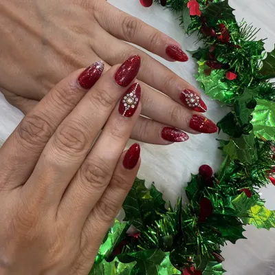 The ultimate Christmas party nails. This look features a rich, sparkly red base on almond nails, with two accent nails adorned with stunning, hand-placed diamond snowflake designs.