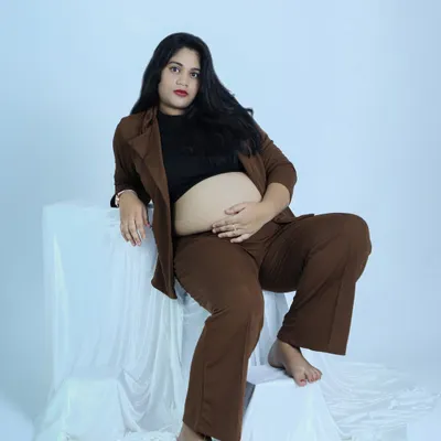 A modern and confident maternity portrait. The mother-to-be wears a stylish brown suit, showcasing her baby bump with a powerful and chic pose in our studio.