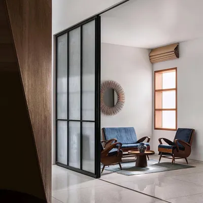 A view into a serene sitting area in the Abhikram residence, where a large sliding glass partition allows for flexible separation of space while maintaining a visual connection to the rest of the home.