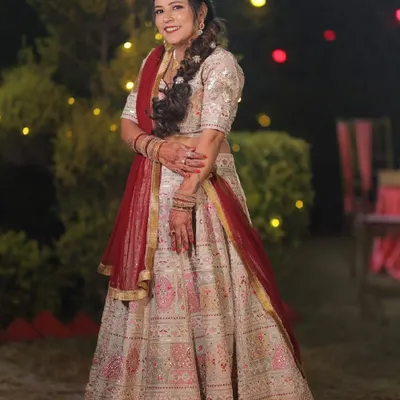 A radiant bride in her custom-made wedding lehenga. The combination of a cream base with intricate pink and red embroidery, paired with a classic red dupatta, creates a timeless and elegant bridal look.