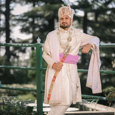 A royal portrait of the groom in his white sherwani, holding a traditional sword. This shot, taken outdoors in Shimla, is full of regal charm.