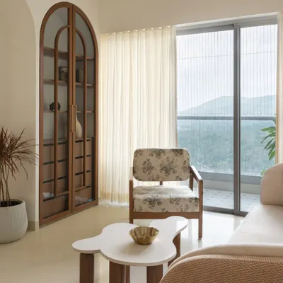 This living area is defined by its serene atmosphere and connection to the outdoors. We used a palette of soft whites and beiges, with an arched wooden cabinet and a floral print armchair adding subtle, timeless charm.