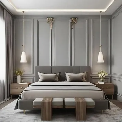 A symmetrical and elegant bedroom design featuring a grey upholstered bed set against a wall with classic panel molding. Matching pendant lights hang over wooden nightstands, and a pair of benches at the foot of the bed completes the sophisticated look.