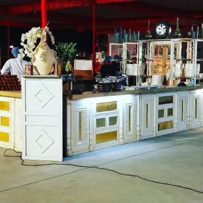 This is one of our custom counter designs, featuring a white and gold theme perfect for an elegant outdoor or sangeet event. The intricate details and built-in shelving allow for a beautiful and functional display.