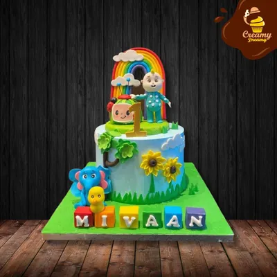 A bright and cheerful Cocomelon cake for a first birthday. This single-tier cake features a rainbow, clouds, and characters from the show, with the birthday boy's name spelled out in colorful blocks.