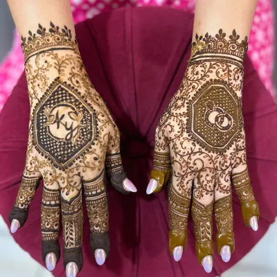 A personalized engagement mehendi featuring the couple's initials 'KY' on one hand and a motif of interlocking wedding rings on the other.