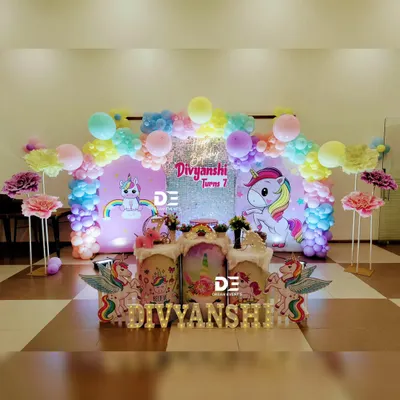 A magical unicorn fantasy for Divyanshi's 7th birthday. This setup features a sparkling backdrop, a rainbow of pastel balloons, and adorable unicorn cutouts, creating a truly dreamy atmosphere.
