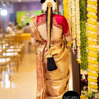 The back view of our client Anusha's bridal look, showcasing the deep back of the cherry red satin blouse and her traditional braided hairstyle.