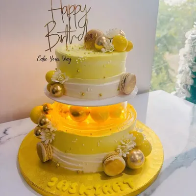 This two-tiered cake was designed for a special birthday, featuring a beautiful yellow and white theme. It's illuminated from within for a magical glow and adorned with golden macarons and delicate sugar flowers.