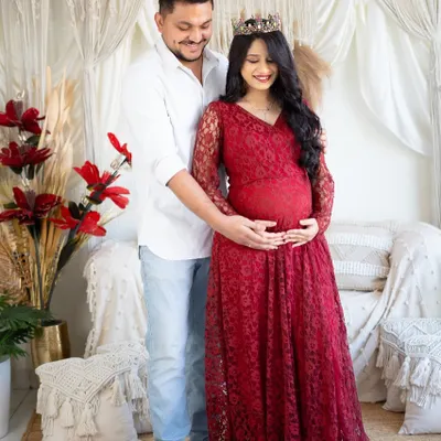 An intimate moment between partners in our boho-chic studio. The mom-to-be wears a beautiful red lace gown while her partner gently holds her, both focused on the baby bump.