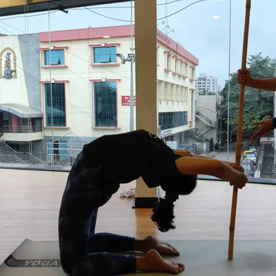 A student uses a stick for support to deepen her Ustrasana (Camel Pose), allowing for a safer and more effective backbend.