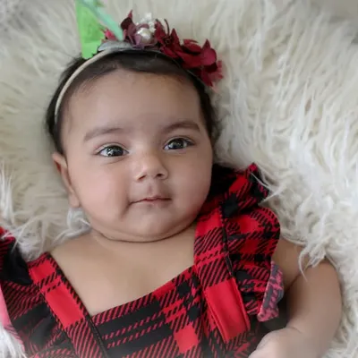 A perfect three-month milestone portrait. This close-up captures her sweet expression and chubby cheeks against a soft, white fur blanket, highlighting the simple beauty of this age.