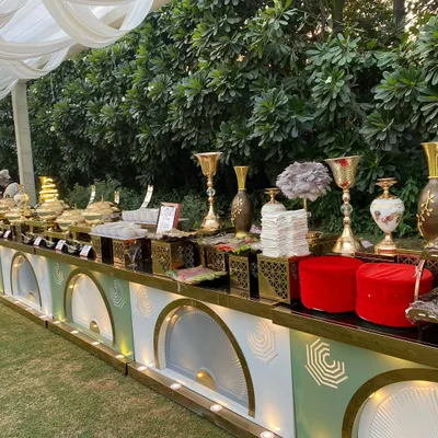 An expansive outdoor buffet line designed for a large gathering. The setup features our signature white and gold art-deco style counters, decorated with floral arrangements and premium brass chafing dishes.