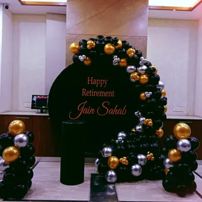 A classy retirement party setup with a black, gold, and silver balloon arrangement around a personalized "Happy Retirement" backdrop.
