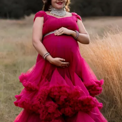 A bright pink ruffled gown stands out beautifully against a natural, grassy background. The layered tulle skirt adds wonderful texture and dimension to this outdoor maternity photo.