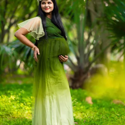 A serene moment in nature. This mom-to-be, wearing a green ombre gown and a floral wreath, looks peaceful and beautiful surrounded by lush greenery.