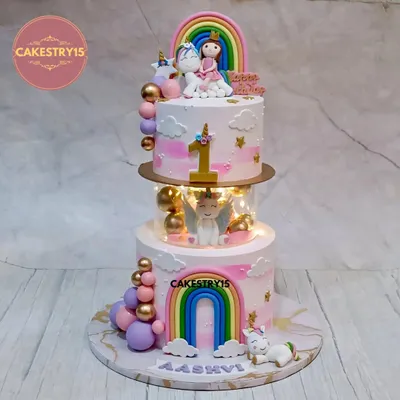 A magical two-tier unicorn cake designed for a first birthday. This choco-vanilla creation features a glowing LED-lit spacer, a fondant unicorn with wings, and charming rainbow decorations.