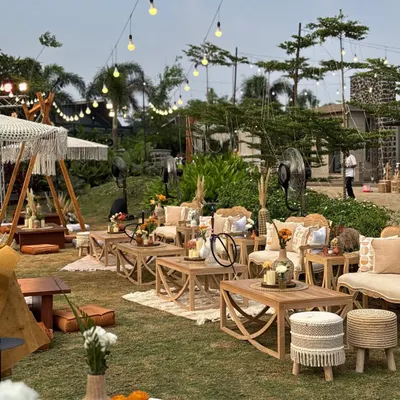 A wide view of a bohemian dreamscape I created. The lawn is filled with various seating arrangements, from low tables with floor cushions to comfortable lounge sets, all under a canopy of twinkling lights.