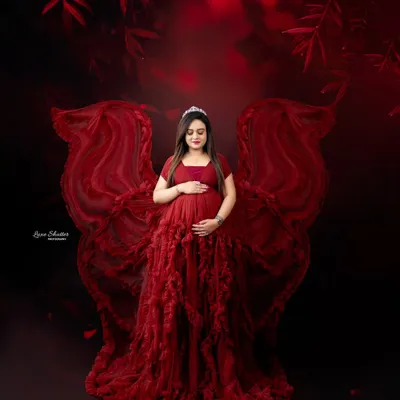 A truly magical portrait of motherhood. This mom-to-be looks like an angel in a deep red ruffled gown, with fabric wings that create a sense of fantasy and wonder.