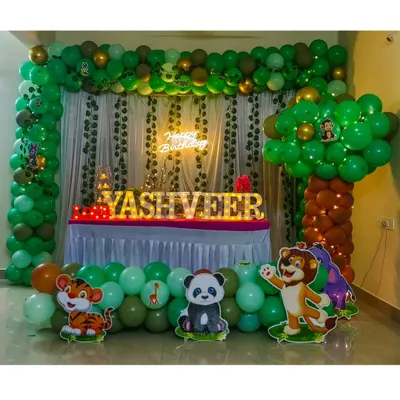 A full jungle theme decoration perfect for a living room setup. This design features a lush green balloon arch with hanging vines, a balloon tree, a neon sign, marquee name lighting, and friendly animal cutouts like a panda, tiger, and lion.