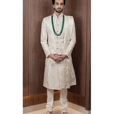 A full view of our ivory sherwani, showcasing its majestic length and the exquisite, subtle embroidery that covers the piece. Paired with a matching stole, it creates a look of pure elegance for a groom.