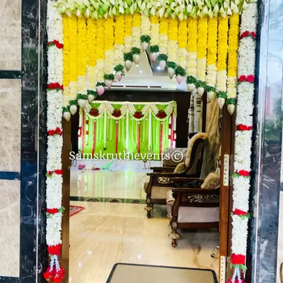A traditional floral archway to welcome guests into your home. This decoration for a main door features garlands of yellow and white flowers, creating an auspicious entrance for a housewarming ceremony.