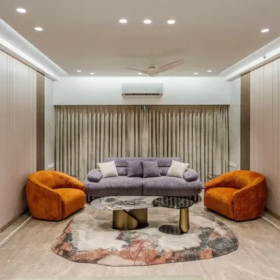 A wide view of a contemporary living room, showcasing a harmonious blend of a lilac sofa and bold orange swivel chairs. The space is defined by seamless, floor-to-ceiling custom millwork and hidden doors, ensuring a clean, uncluttered look.