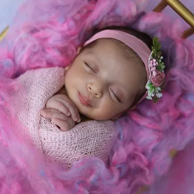 A perfect sleepy smile on a baby girl, swaddled in pink and nestled in a bed of soft, colorful wool. This is a classic, heartwarming newborn portrait that parents adore.