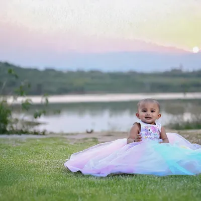 A beautiful outdoor portrait of a baby girl in a princess dress, with the sunset over a lake in the background. The natural light at golden hour is simply magical.
