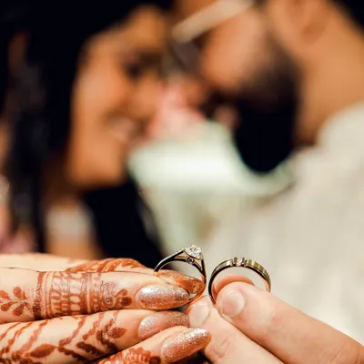 A creative shot of the wedding rings held by the couple. The focus is on the rings, with the couple blurred lovingly in the background, symbolizing that their union is at the center of it all.