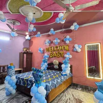 A classic 'Welcome Baby' room decoration for a baby boy. The setup includes blue and white balloons on the ceiling and walls, with foil balloons spelling out 'WELCOME BABY' over the bed.