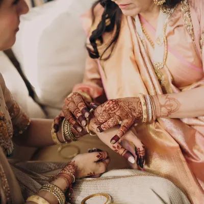 The mothers have seen it all. We celebrate the OG icons, styling them in quiet luxury that reflects their grace and wisdom. Here, a mother helps her daughter with her bangles, a timeless moment of connection.