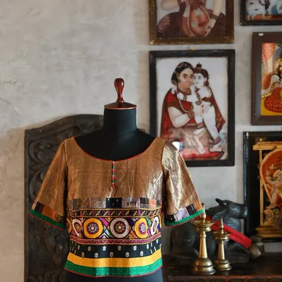 This custom-made kurti-style blouse is designed to be paired with sarees or skirts. The front features antique gold linen silk and a panel of hand-done Kutch embroidery.