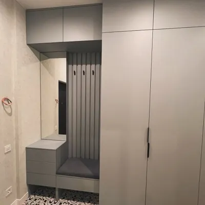 A perfect example of an integrated entryway unit. This piece combines a full-height wardrobe with a comfortable seating nook, coat hooks, a mirror, and drawers, creating a highly functional and organized welcome to the home.