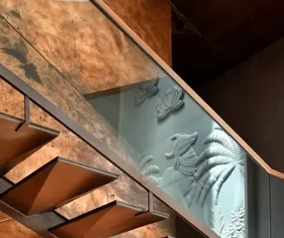 This copper and metal staircase is a study in lightness and intensity. The cantilevered treads seem to float, while the glass balustrade offers a glimpse of the traditional 'pichwai' relief art on the wall, lit by a skylight above.