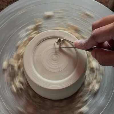 Trimming a piece on the wheel. This is a crucial step to refine the base and shape of a pot after it has hardened slightly.