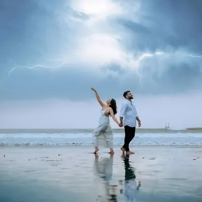A truly epic and dramatic pre-wedding shot. The couple stands on the wet sand as lightning strikes across the stormy sky, creating a powerful and unforgettable image of their love.