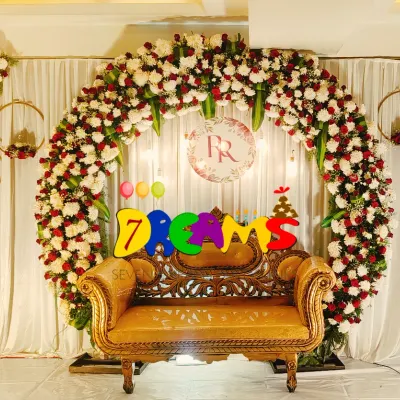I designed this symmetrical stage decoration for a wedding event. It features a large floral arch of red and white flowers, with smaller hanging floral rings on either side for a balanced and grand look.