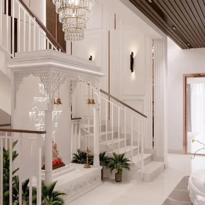 A magnificent white mandir beautifully integrated under a staircase. The intricate jali work, traditional temple design, and elegant chandelier create a divine and serene atmosphere.