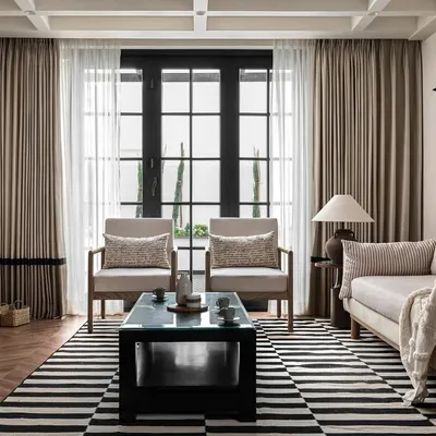 The living room of our 'Riviera Maison' project, inspired by the French Riviera. The design uses a calm, neutral palette, classic furniture silhouettes, and a bold striped rug to create a space that is both sophisticated and relaxed.
