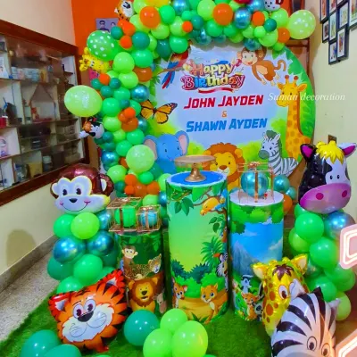 A vibrant jungle-themed birthday party setup. This decoration includes a large circular backdrop with jungle animals, themed pedestals for the cake, animal-shaped foil balloons, and a lush green balloon arch.