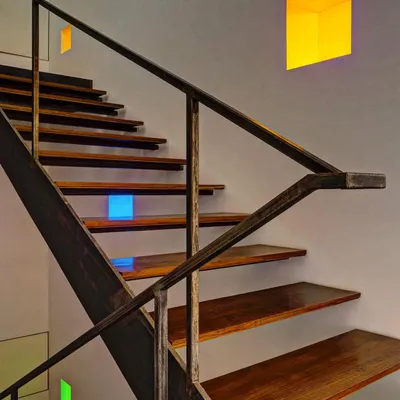 This staircase explores the intersection of light, detail, and materiality. The warmth of the wooden treads contrasts with the industrial feel of the steel railing, while small, colored light niches add a playful detail.