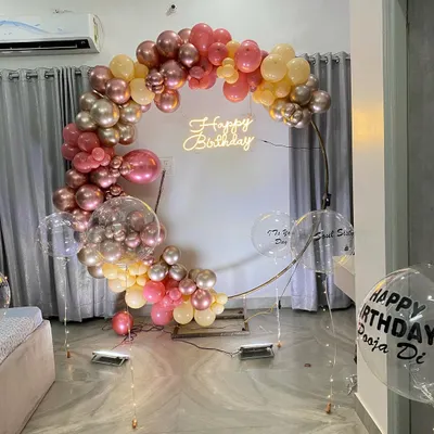 An elegant balloon ring decoration for an intimate home celebration. This setup features a half-arch of chrome and pastel balloons on a golden ring, with a 'Happy Birthday' neon sign.