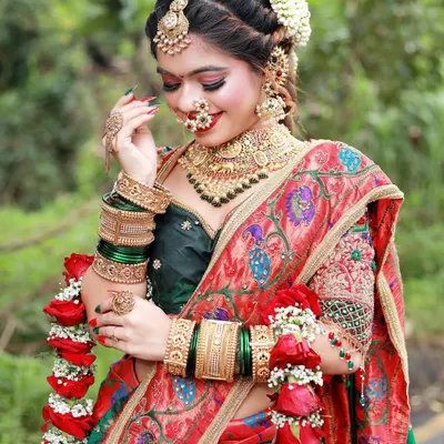 A beautiful bride adorned with fresh red and white flower garlands (Varmala) and a traditional braided hairstyle. The look is completed with classic gold jewelry and a joyful expression.