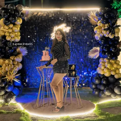 A perfect example of a modern glam setup. A sparkling shimmer wall, black and gold balloon arrangements, and a custom neon sign create a high-impact photo corner.