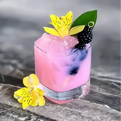 A beautifully crafted pink mocktail. This drink is garnished with an edible flower and fresh blackberries, showcasing our flair for creating visually appealing non-alcoholic beverages.