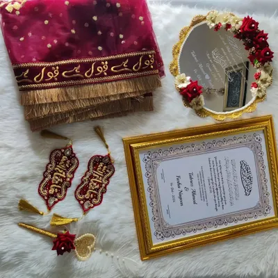 Here is a complete Nikah set laid out, featuring a maroon 'Qubool Hai' dupatta, a custom-framed marriage certificate, a floral-decorated mirror, and embroidered Iman Zamins. Every piece is designed to complement the others.