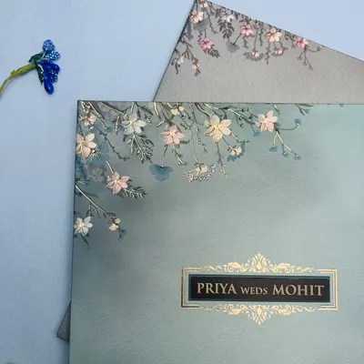 A closer look at this serene, pastel blue invitation. The delicate floral sketches and gold foil nameplate create a look of understated luxury, perfect for a modern romance.
