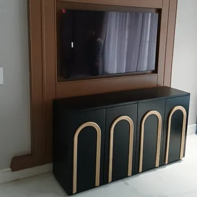 A striking black media cabinet with applied arch details in a gold finish. This piece was designed as part of a larger TV unit, providing stylishly concealed storage that complements the room's modern aesthetic.